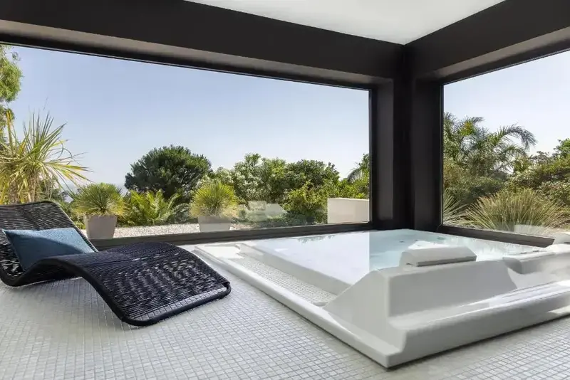 Un jacuzzi intégré dans une pièce lumineuse donne sur une végétation luxuriante.