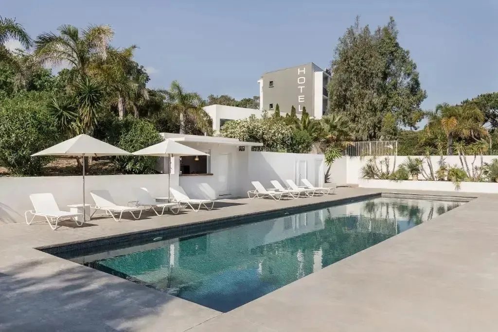 Une piscine rectangulaire bordée de transats blancs sous des parasols.