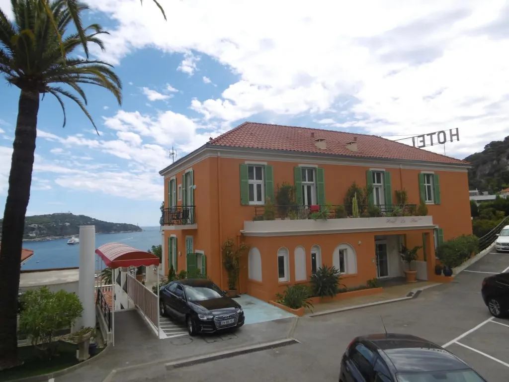 Bâtiment orange à deux étages avec des volets verts et une vue sur la mer.