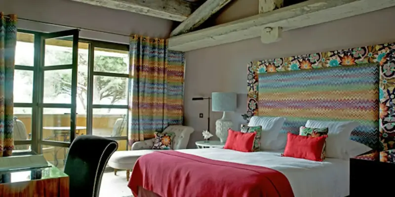 Une chambre lumineuse avec un grand lit décoré de coussins colorés et un accès à une terrasse.