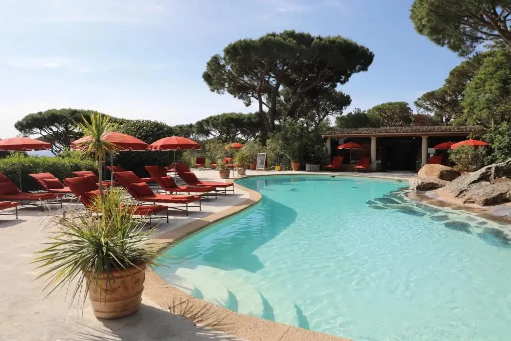 Une piscine bordée de transats rouges sous des parasols, entourée de végétation luxuriante.