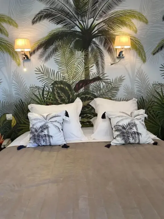 Un lit double est dispose devant un mur decoratif avec des palmiers.