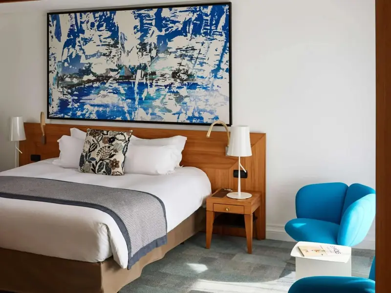Une chambre lumineuse avec un grand tableau abstrait au-dessus du lit.