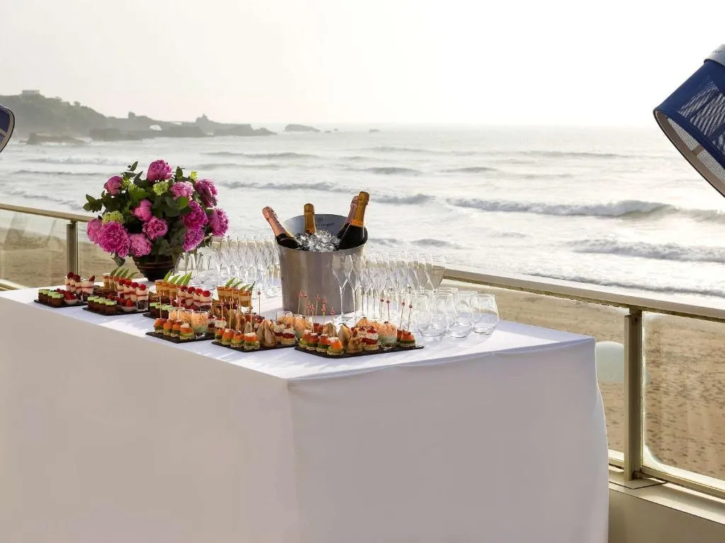 Une table dressée de mets et de boissons offre une vue sur l'océan.