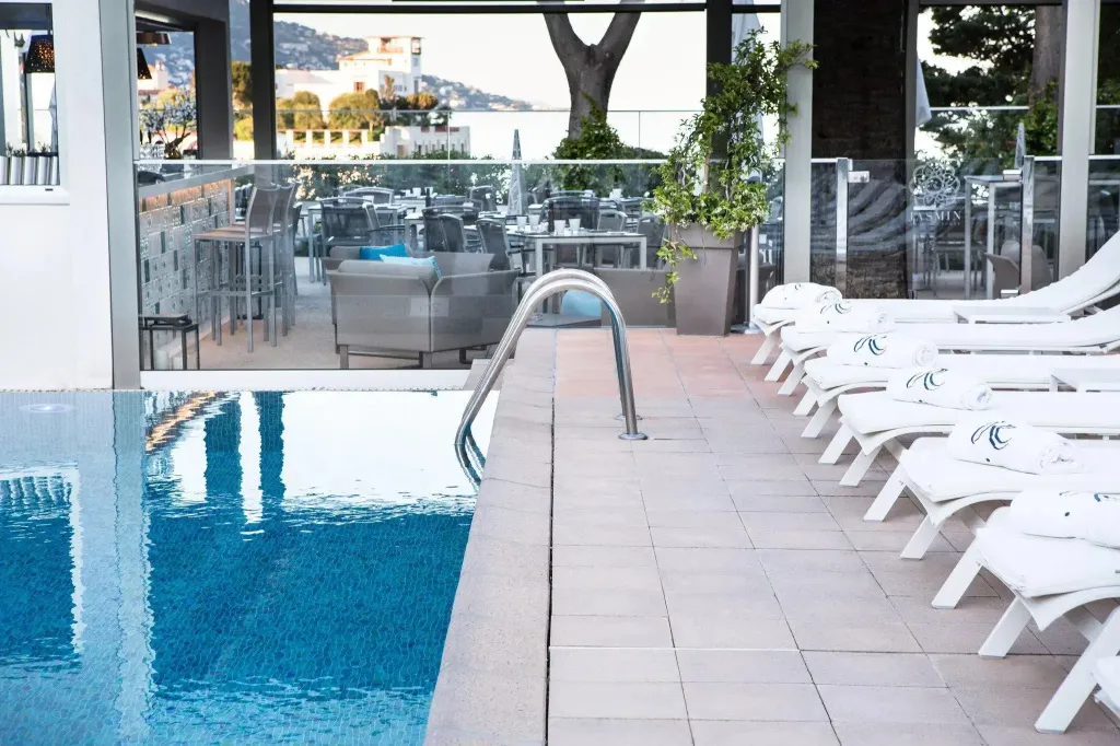 Transats blancs alignés au bord d'une piscine turquoise avec vue sur la mer.
