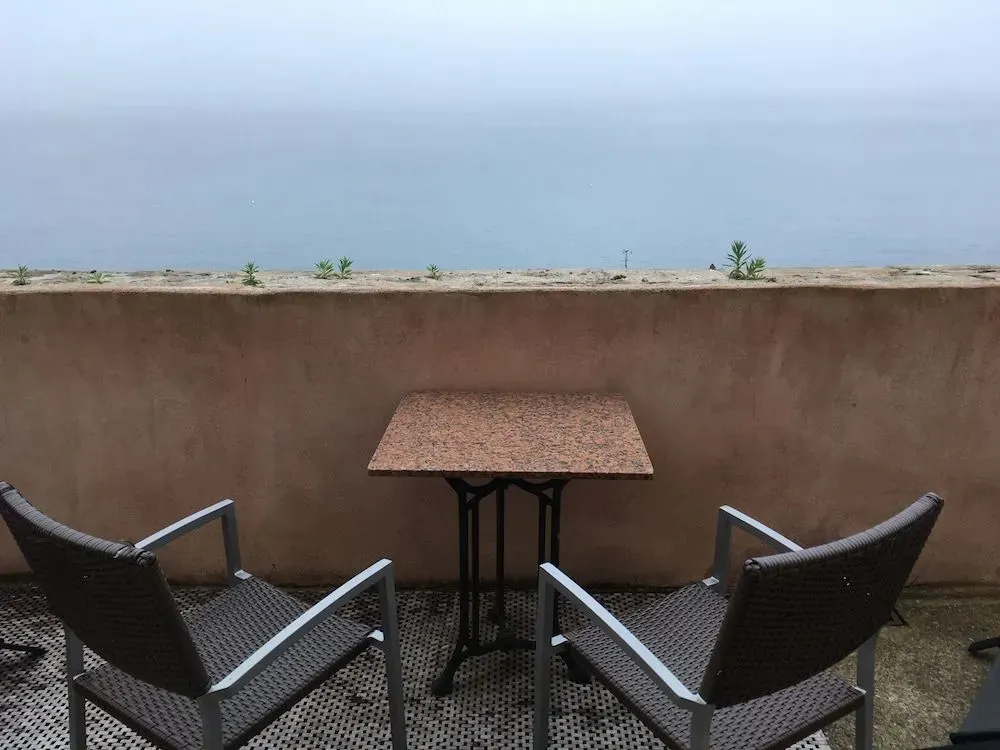 Une table et deux chaises sont disposées sur une terrasse avec vue sur la mer.