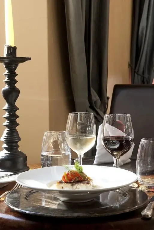 Une assiette de poisson est présentée sur une table dressée avec des verres à vin et une bougie.