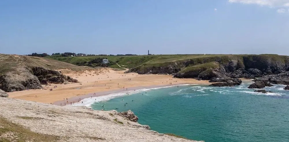 Une plage de sable fin bordée d'une eau turquoise et de falaises verdoyantes.