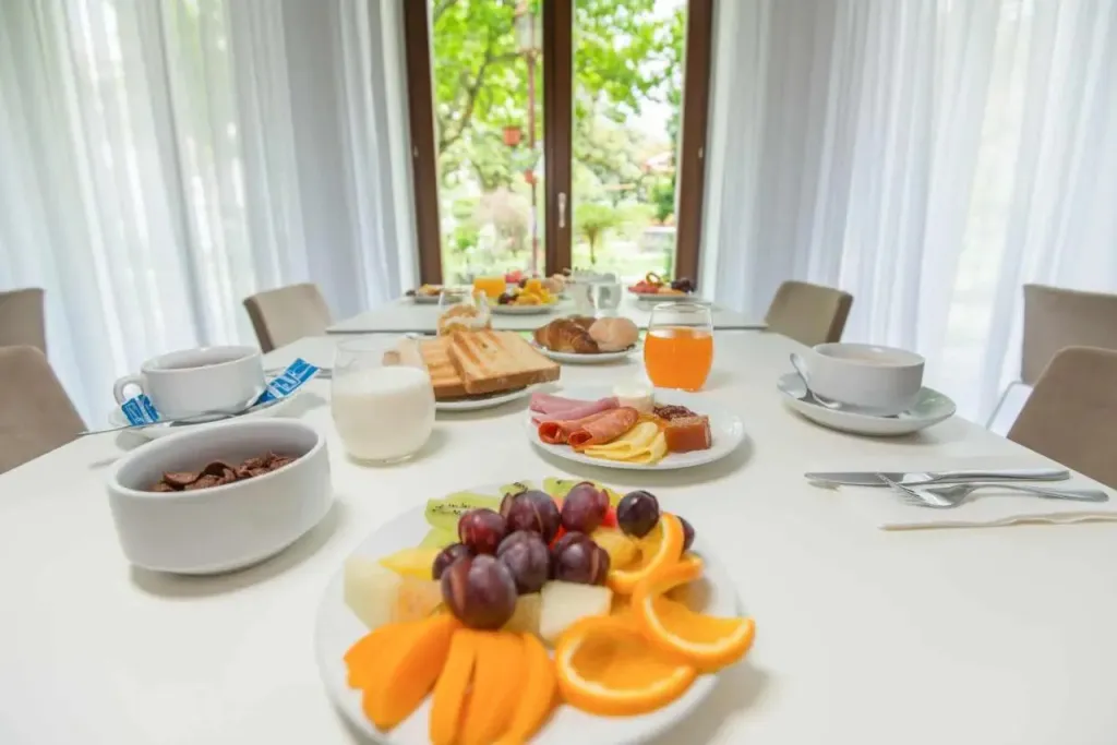 Une table est dressée avec un petit-déjeuner composé de fruits, de viennoiseries et de boissons.