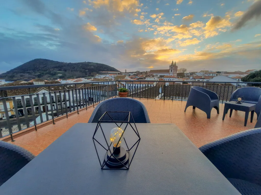 Terrasse aménagée avec tables et chaises offrant une vue sur la ville et le coucher de soleil.