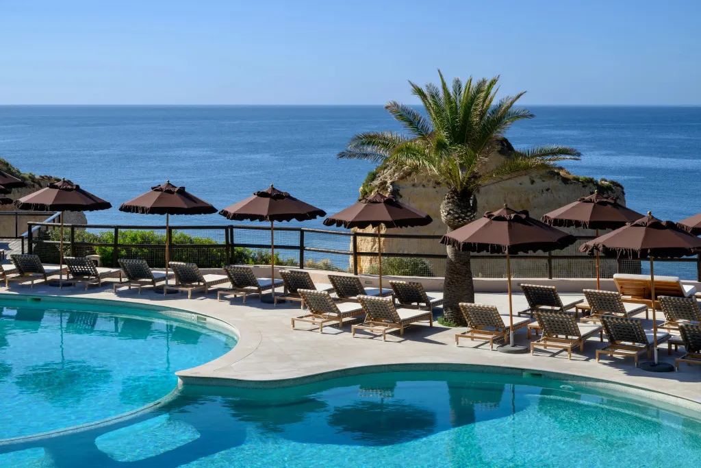 Transats et parasols bordent une piscine avec vue sur la mer.