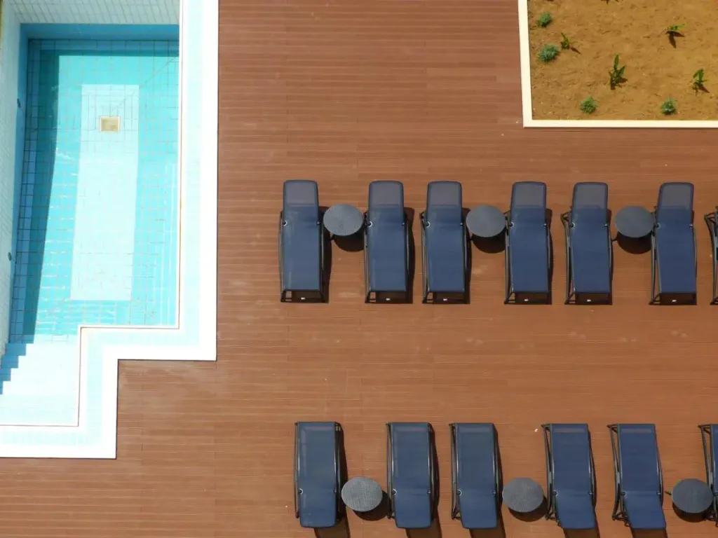 Transats alignés sur une terrasse en bois près d'une piscine rectangulaire.