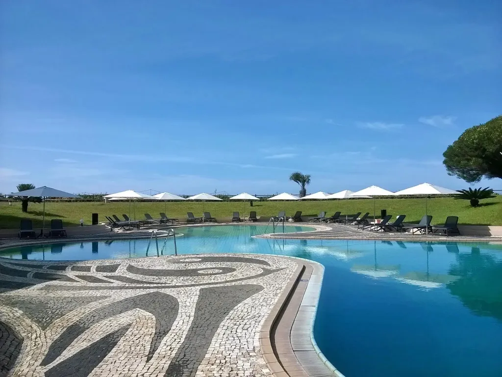 Piscine extérieure avec transats et parasols sous un ciel bleu.