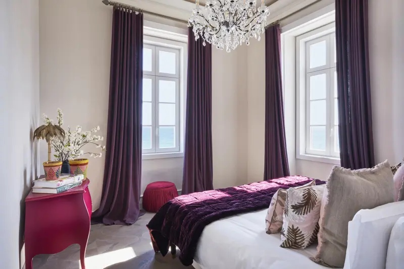 Une chambre lumineuse avec un lit recouvert d'une couverture violette et des oreillers décoratifs.
