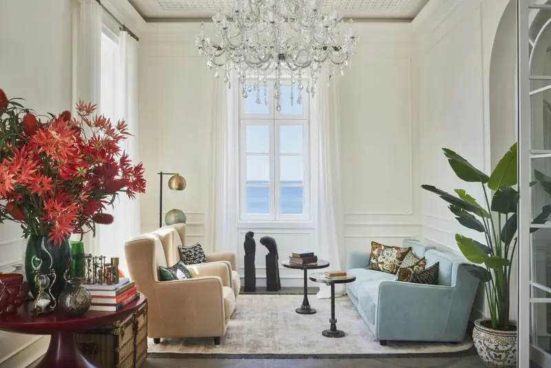 Un salon clair et spacieux avec des fauteuils et un canapé face à une fenêtre donnant sur la mer.