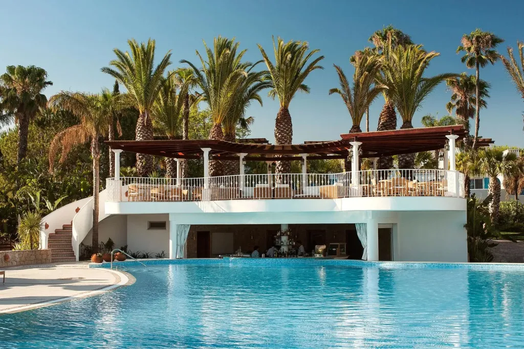 Une piscine turquoise bordée d'une terrasse ombragée avec un bar en contrebas.
