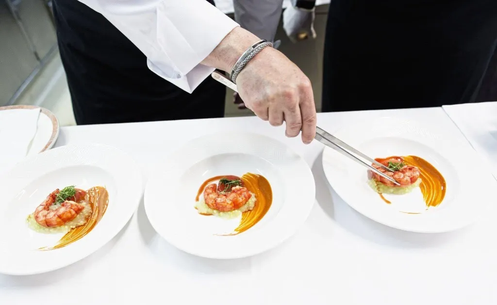 Une personne en tenue de cuisine dresse des assiettes de crevettes.