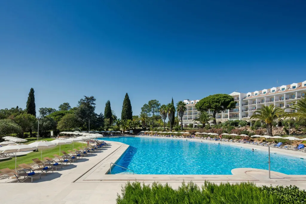 Une grande piscine rectangulaire bordée de transats dans un complexe hôtelier.