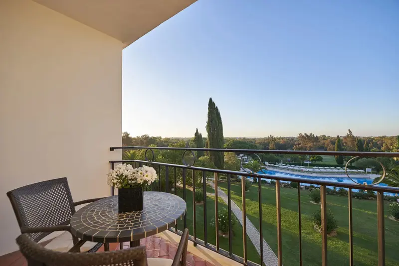 Balcon avec table et chaises donnant sur un jardin verdoyant et une piscine.