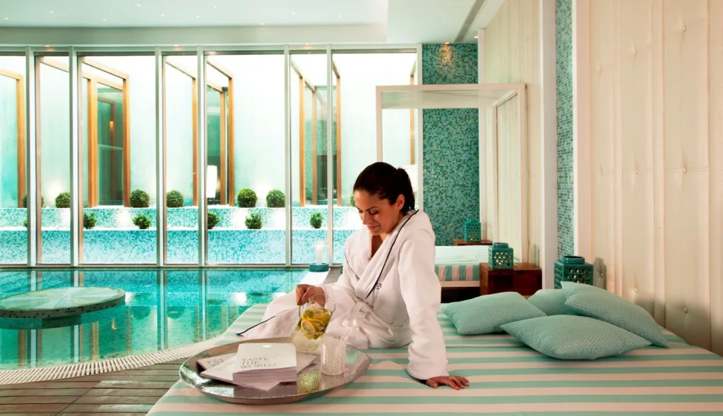 Une femme se détend près d'une piscine intérieure avec un plateau de boissons.