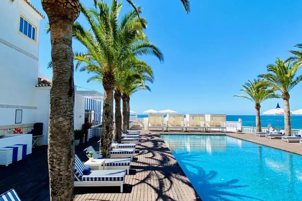 Transats alignés au bord d'une piscine ensoleillée avec vue sur la mer.