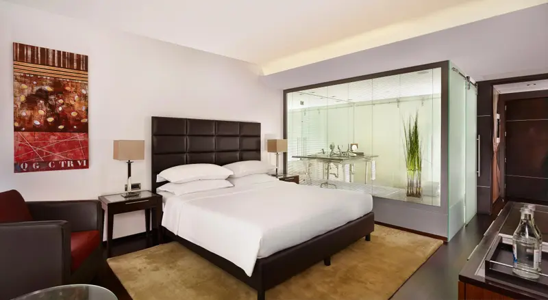 Une chambre lumineuse avec un grand lit et une salle de bain vitrée.