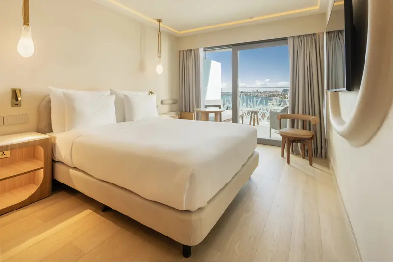 Une chambre lumineuse avec un grand lit et un accès à un balcon.