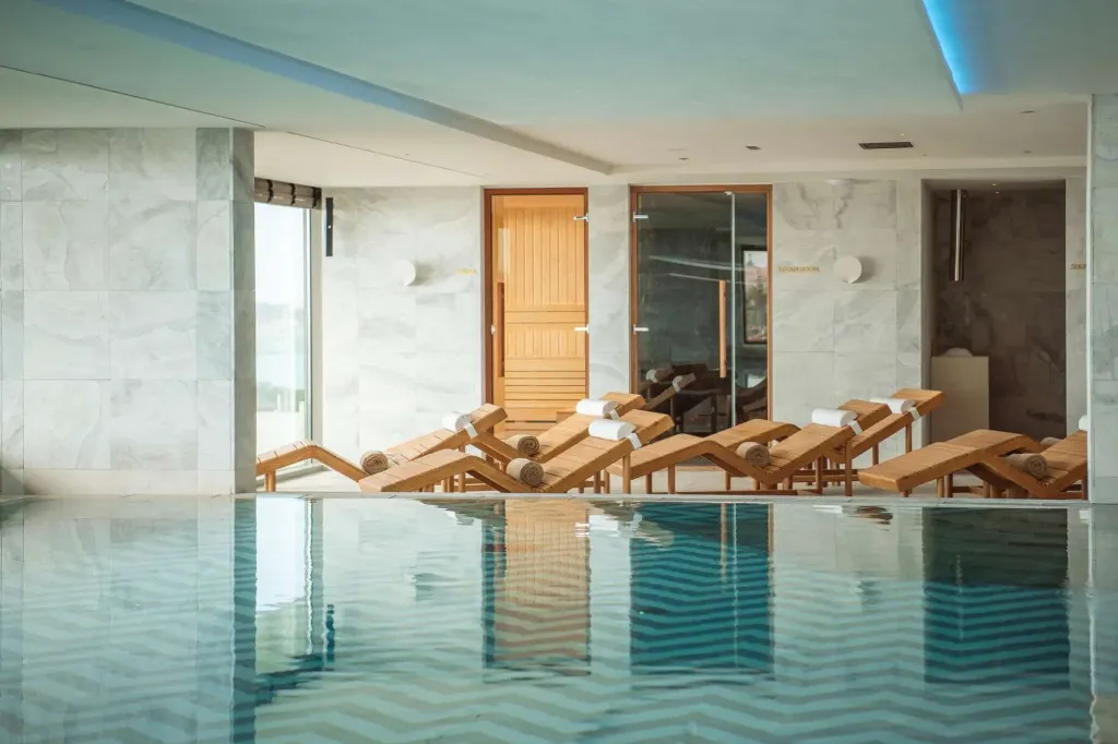Transats alignés au bord d'une piscine intérieure lumineuse.