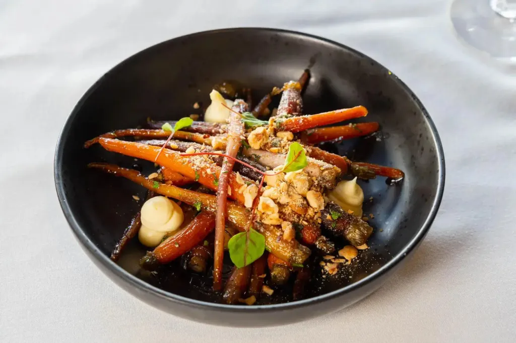 Assiette de carottes glacées agrémentées de noix et d'une sauce crémeuse.