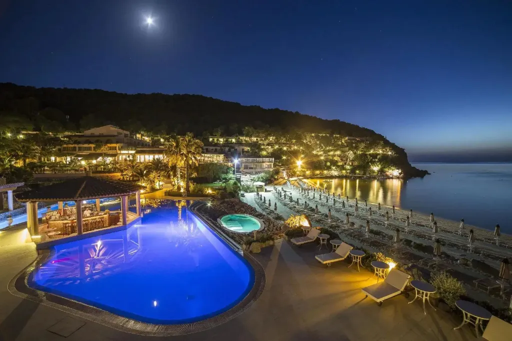 Vue nocturne sur une piscine illuminée et une plage bordée de transats.