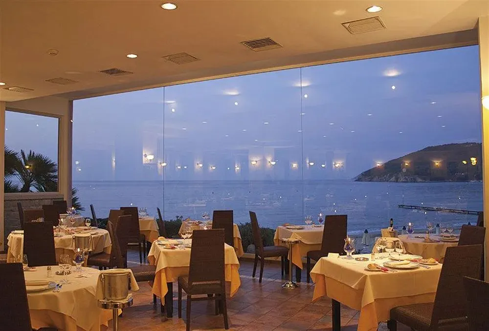 Une salle lumineuse avec des tables dressées face à la mer.