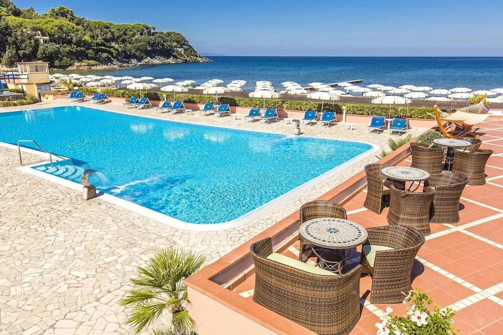Une piscine bleue bordée de chaises longues et de parasols, avec une vue sur la mer.