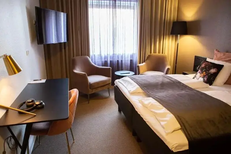 Une chambre d'hôtel lumineuse avec un bureau, des fauteuils et un lit.