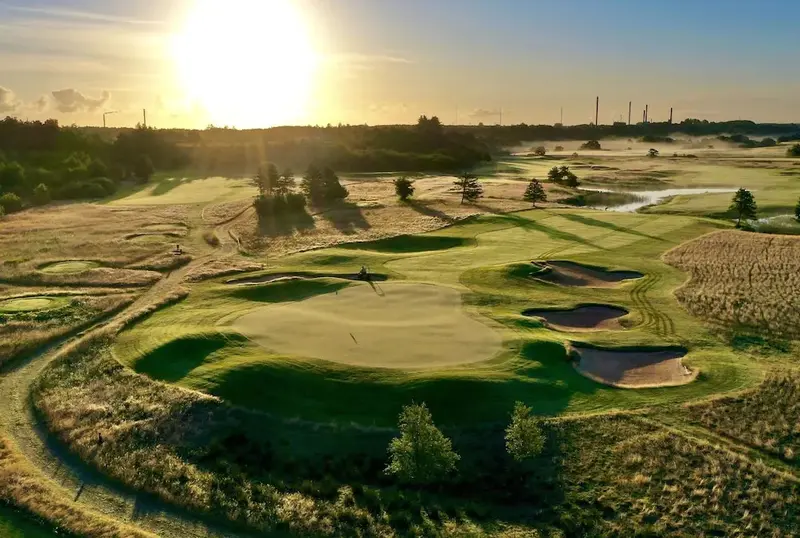 Un terrain de golf verdoyant s'étend sous un ciel ensoleillé et brumeux.