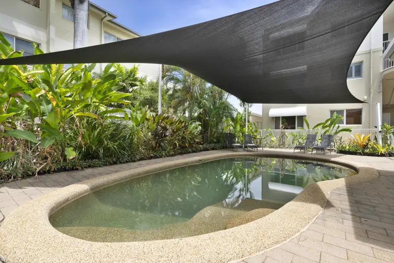 Piscine ensoleillée ombragée par une voile d'ombrage et entourée de végétation luxuriante.