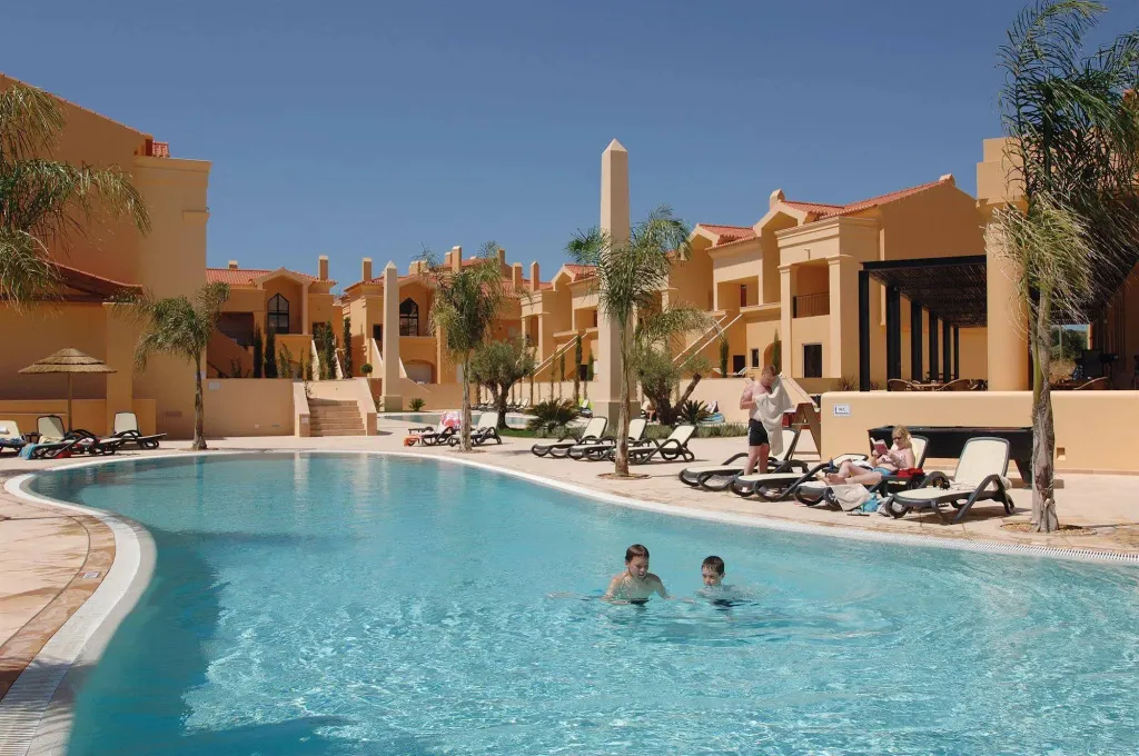 Une piscine bordée de transats dans un complexe hôtelier ensoleillé.