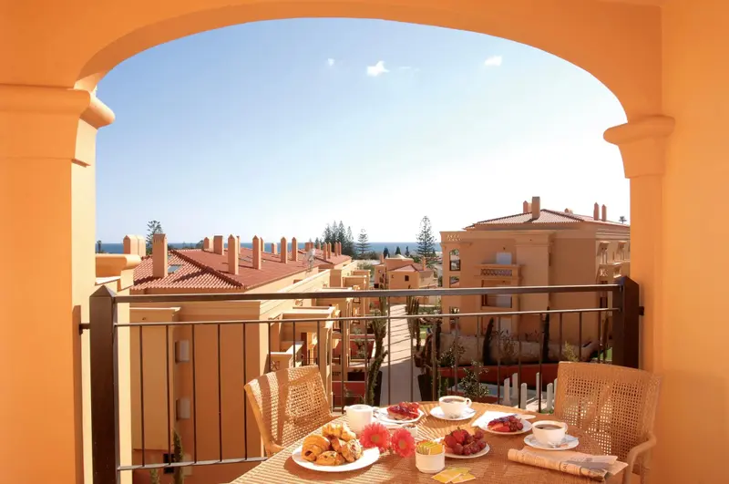Une table est dressée pour le petit-déjeuner sur un balcon avec vue sur les toits et la mer.