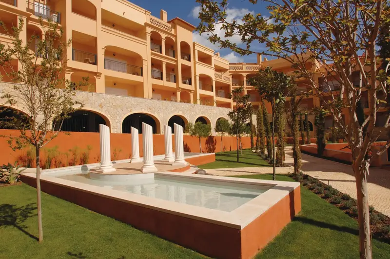 Jardin soigné avec fontaine et bâtiment aux balcons colorés.