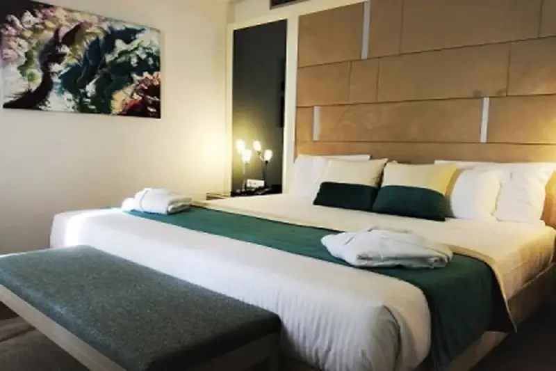 Une chambre lumineuse avec un grand lit recouvert d'une courtepointe verte et de coussins.