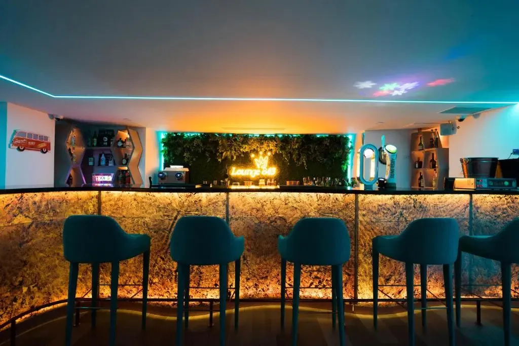 Un comptoir de bar illuminé avec des tabourets bleus et un mur végétal.