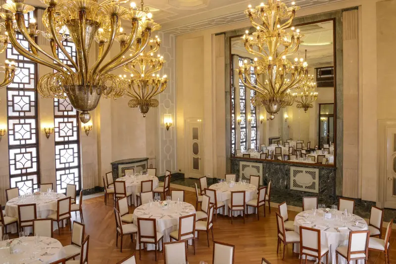 Une salle lumineuse est aménagée avec des tables rondes nappées et des chaises.