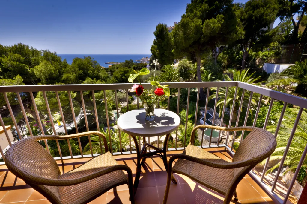 Une table et deux chaises en osier sur un balcon fleuri avec vue sur la mer.