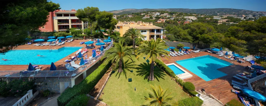 Deux piscines avec transats et parasols dans un complexe hôtelier ensoleillé.