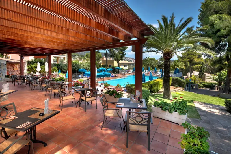Une pergola ombrage une terrasse avec des tables et des chaises.