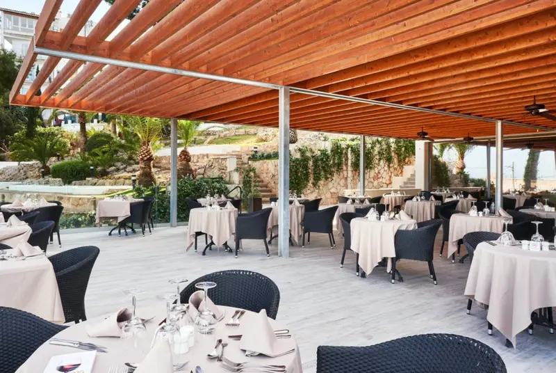 Une terrasse ombragée abrite des tables de restaurant dressées pour le service.