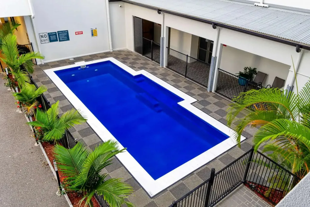 Une piscine rectangulaire bleue entourée d'une terrasse pavée et de végétation tropicale.