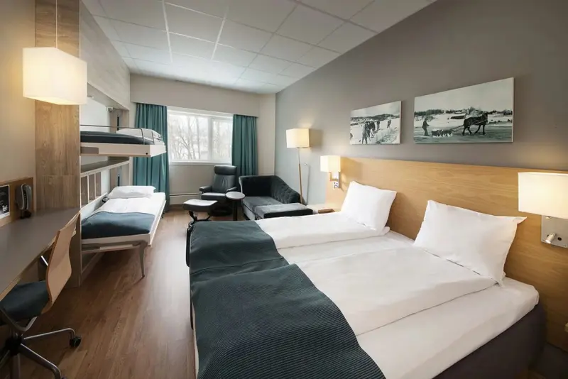Une chambre avec un lit superposé et deux lits simples, éclairée par des lampes.