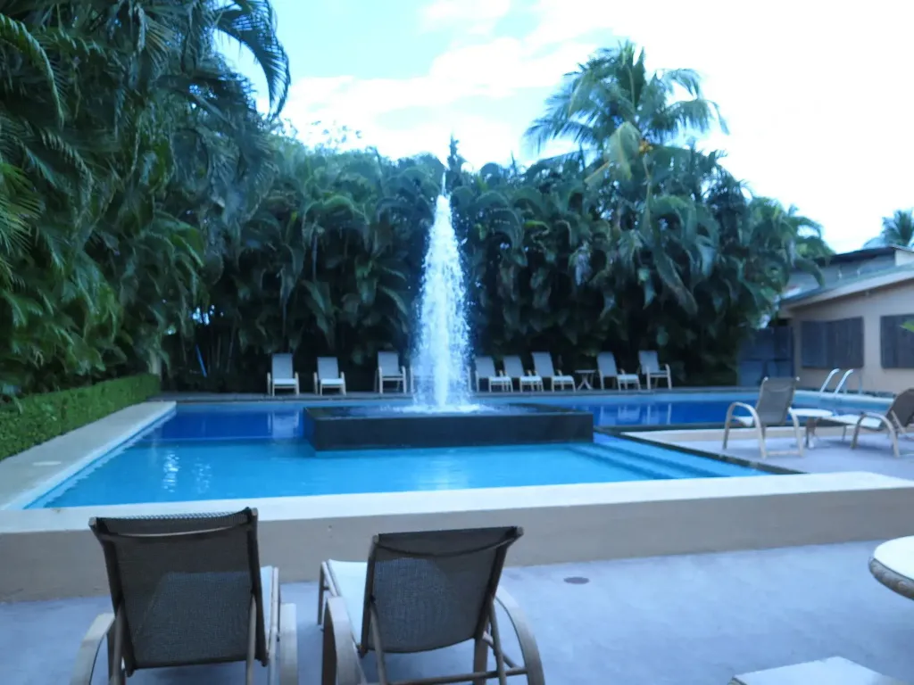 Une piscine rectangulaire avec une fontaine centrale et des transats.