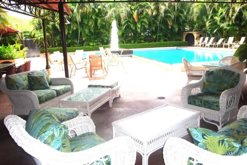 Espace de détente extérieur avec mobilier en osier près d'une piscine.