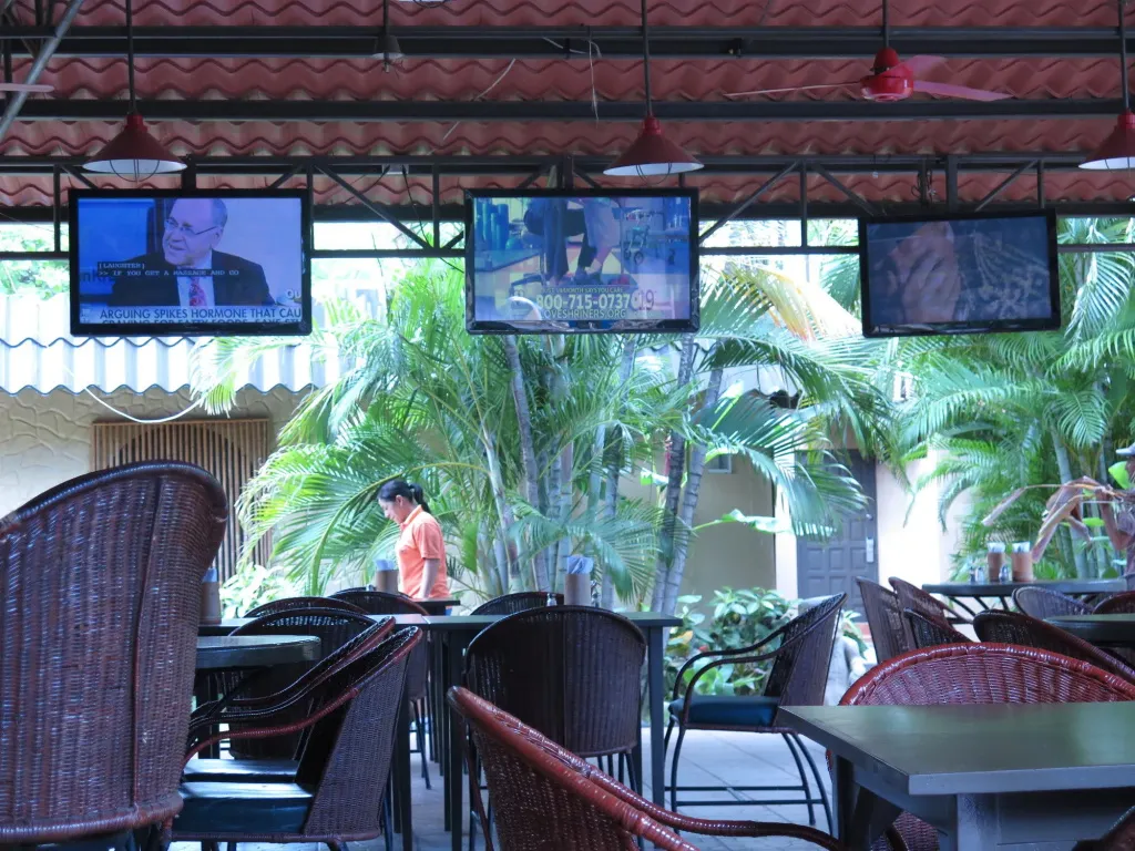 Espace extérieur ombragé avec des tables et des écrans de télévision.